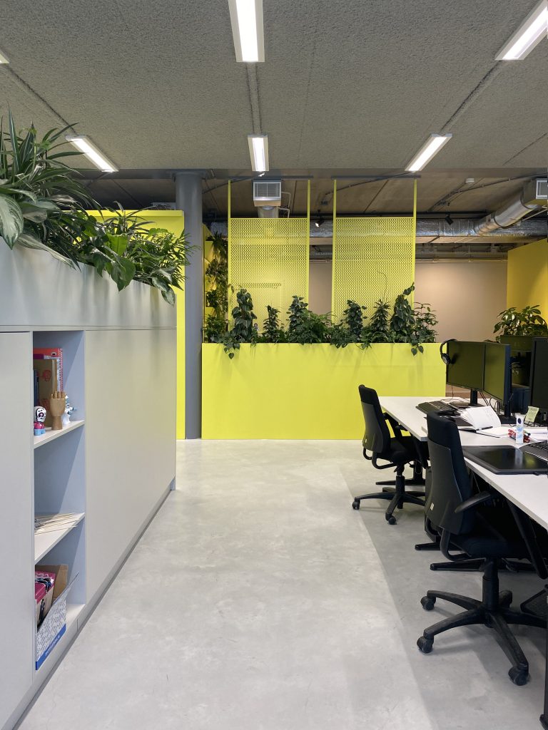 doorkijkje naar loungehoekje, gele dividers met staal en veel planten, werkplekken